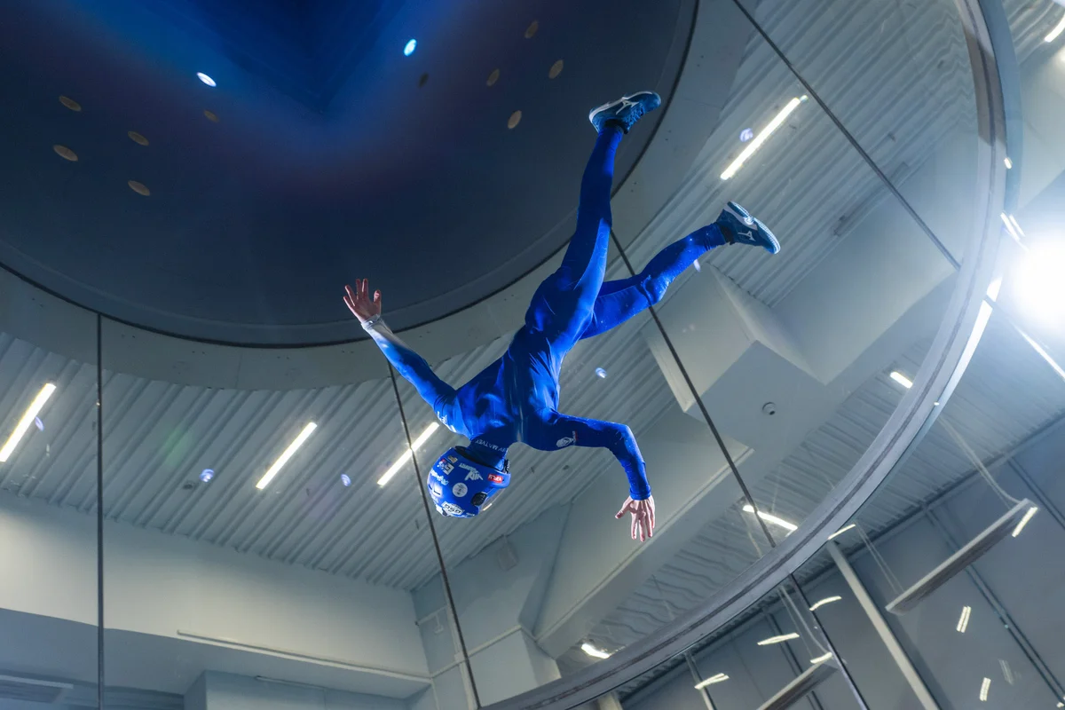 Kuzbas Arena में TT52 Pro के अंदर, एक पेशेवर एथलीट सटीक हेड-डाउन पैंतरेबाज़ी करता है, जो टनल की असाधारण प्रवाह गुणवत्ता (flow quality) को प्रदर्शित करता है। 5.2 मीटर के उड़ान कक्ष में TunnelTech का विशेष रूप से निर्मित गोल, मल्टी-लेयर ग्लास लगा है, जो न केवल शोर को सोखता है बल्कि दर्शकों और कोचों के  लिए स्पष्ट दृश्यता भी सुनिश्चित करता है। ऊपर की ओर डिफ्यूज़र (diffuser) का निर्बाध संक्रमण, जिसे एकीकृत एलईडी लाइटिंग द्वारा हाइलाइट किया गया है, सिस्टम के स्वच्छ वायुगतिकीय डिजाइन को दर्शाता है।