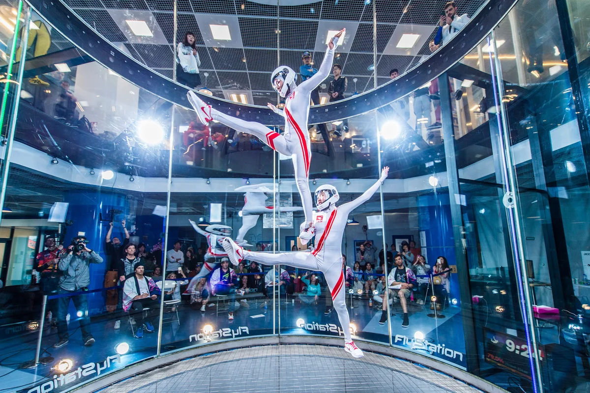 Dwóch flyerów wykonuje zsynchronizowany manewr freestyle wewnątrz komory lotu TT45 PRO w FlyStation Japan. Sportowcy tworzą zrównoważoną formację bezpośrednio nad stalową siatką bezpieczeństwa o niskim oporze. Tunel aerodynamiczny o średnicy 4,5 metra posiada bezramowe ściany ze szkła wielowarstwowego (multilayer glass), co pozwala widzom oglądać występ zarówno z parteru, jak i z górnej antresoli. Obiekt ten, oddany do użytku (commissioned) w 2017 roku, obsługuje profesjonalne zawody, takie jak Sakura Cup, zapewniając stabilny strumień objętościowy powietrza (airflow) o dużej prędkości, odpowiedni dla zaawansowanych dyscyplin dynamic i latania artystycznego.