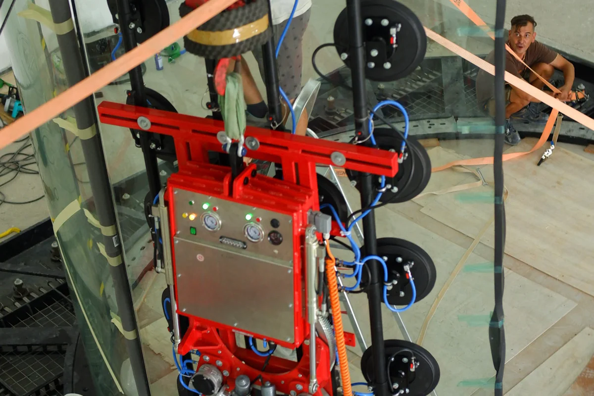 Nuestro equipo técnico instala un panel de vidrio multicapa curvo para el túnel de viento TT45 PRO en las instalaciones de Brimob en Indonesia. Un elevador de vacío de alta resistencia asegura la sección transparente mientras los operarios la guían hacia su posición sobre la red de seguridad. Así se construye la cámara de vuelo de 4,5 metros de diámetro, utilizando vidrio reforzado químicamente para garantizar la máxima seguridad contra impactos y claridad óptica en entrenamientos profesionales.