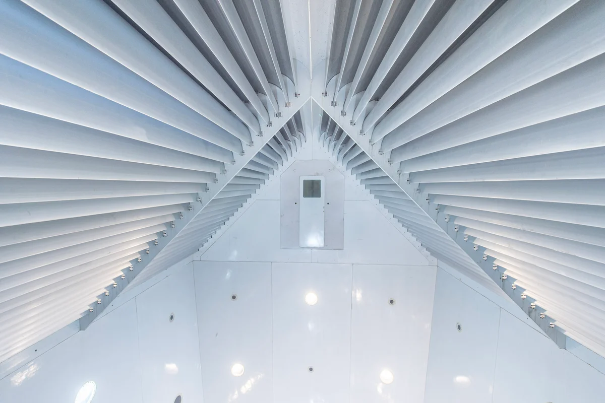 Ang mga aluminum turning vanes ay nakaposisyon sa itaas ng flight chamber sa FlyStation Japan. Ang mga vanes ay bumubuo ng V-shaped na istraktura na dinisenyo upang hatiin ang airflow sa dalawang agos na nakadirekta sa kaliwa at kanang return ducts. Ang pinto na matatagpuan sa gitna ng assembly ay ang pasukan sa base jumping chamber, na nagpapahintulot ng mga pagtalon sa flight zone mula sa taas na halos 20 metro.