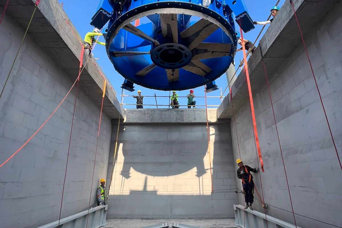 O macara de mare tonaj coboară o unitate de ventilator axial (Axial fan) EVG albastră în canalul de retur (Return duct) vertical din beton al unui tunel aerodinamic (Wind tunnel) TT43 Smart la facilitatea China Flight Town. Ansamblul ventilatorului, având palete din fibră de carbon (Carbon-fiber blades), coboară spre o structură staționară de palete directoare (Guide vanes) poziționată la baza puțului. Tehnicienii de instalare ghídează sarcina folosind tehnici de acces cu corzi pentru a asigura alinierea precisă în interiorul carcasei de beton. Această etapă de instalare plasează componentele principale de generare a debitului de aer (Airflow) în structura buclei de retur.