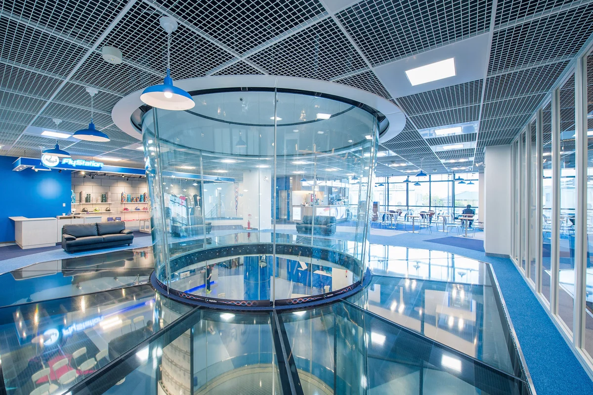 A FlyStation Japan ezen belső nézete a TunnelTech TT45 Pro repülőkamra felső szakaszát mutatja be. Egy szerkezeti üvegpadló veszi körül a csatornát, függőleges rálátást biztosítva a repülési területre és az alsó szintekre. A telepítés ívelt többrétegű üveg paneleket használ a repülőkamra falaihoz. A környező kereskedelmi tér magában foglal egy FlyStation márkajelzéssel ellátott recepciót, kiskereskedelmi polcokat és n ézőtéri üléseket, bemutatva a szélcsatorna infrastruktúrájának integrációját a létesítmény nyilvános zónájába.