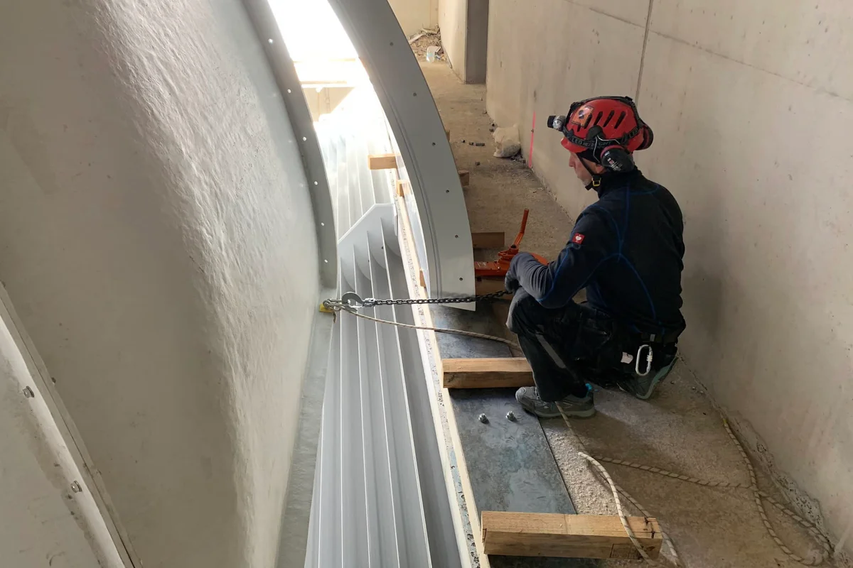 Fundi anaweka sehemu iliyopinda ya duct ya kompositi ya FRP iliyo na turning vanes wakati wa kuunganisha handaki la upepo la Luxfly. Kipengele hiki huunda kona ya mzunguko wa TT45 PRO recirculating loop, iliyoundwa kuelekeza upya mtiririko wa hewa ndani ya muundo wa saruji. Mchakato wa ufungaji unahusisha mpangilio sahihi wa ductwork ya kompositi kwa kutumia minyororo ya rigging ili kutoshea bahasha ya jengo.