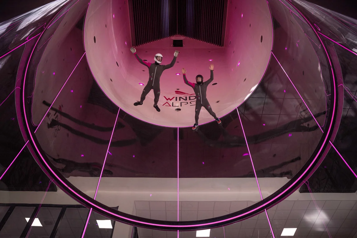 Hai người bay đang thực hiện kỹ thuật belly flying trong buồng bay TT45 PRO tại cơ sở Wind Alps, Pháp. Góc nhìn từ dưới lên làm nổi bật công nghệ của TunnelTech: phần kính hình trụ đường kính 4,5m được chế tạo từ kính nhiều lớp hấp thụ âm thanh tròn hoàn hảo. Thiết kế không khung này mang lại tầm nhìn không biến dạng, lý tưởng cho huấn luyện chuyên nghiệp và bay nhóm.