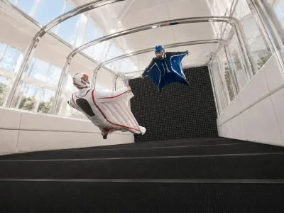 Two wingsuit pilots flying side by side inside the inclined glass flight chamber of the Banana WS